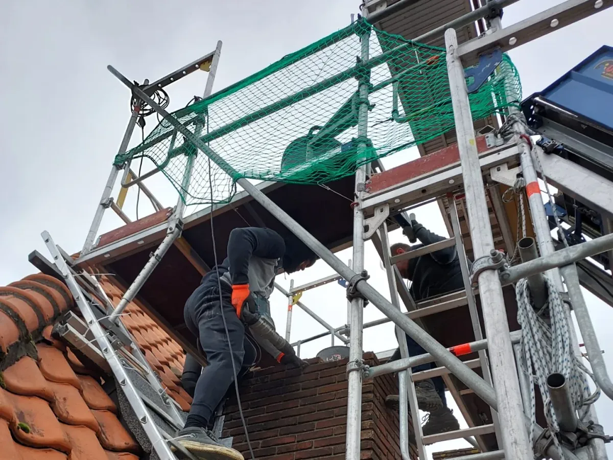 Werk aan een gemetselde schoorsteen vanaf een steiger.