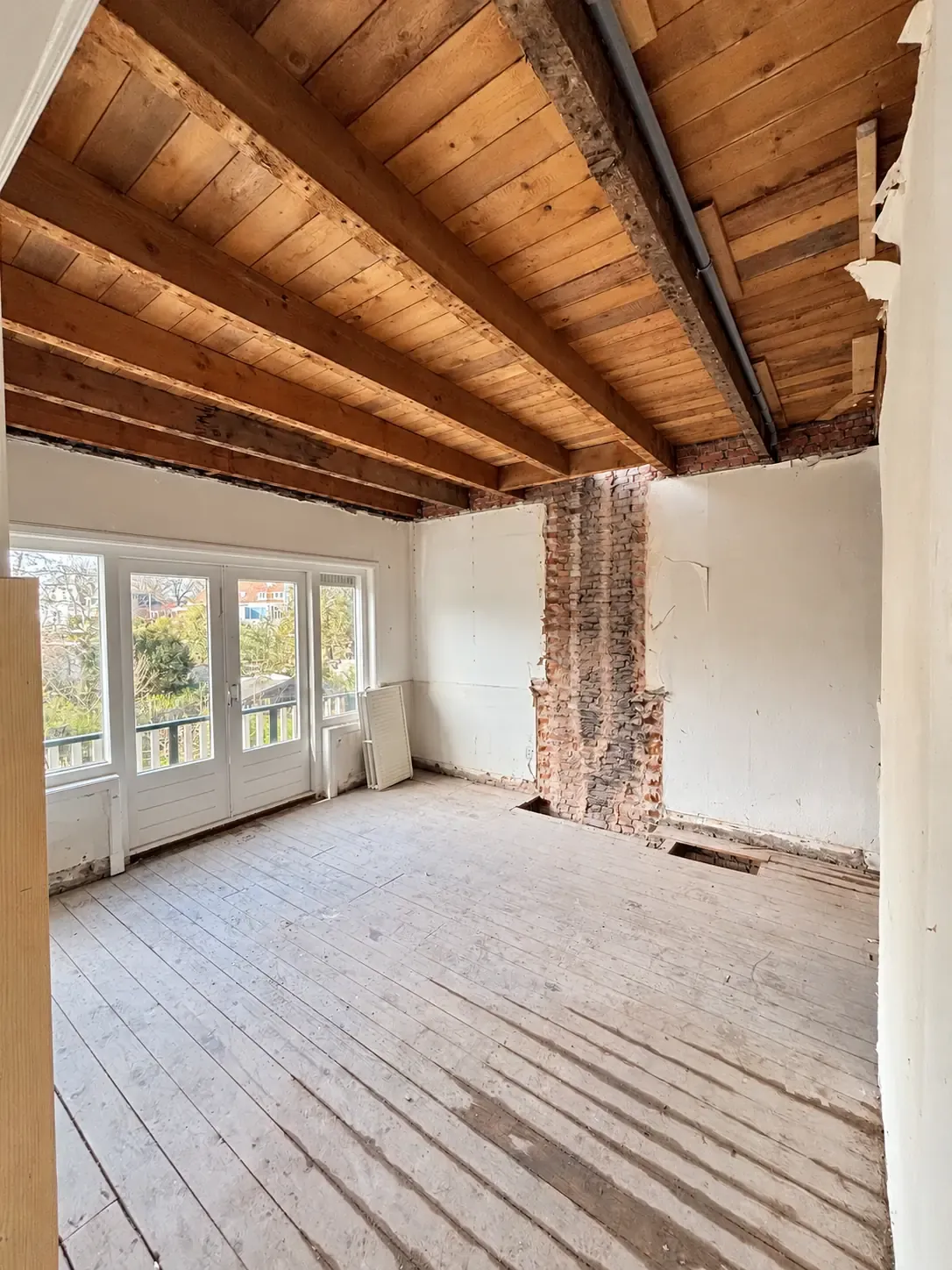 Een woninginterieur met vrijgelegde houten balken en verwijderde afwerking.